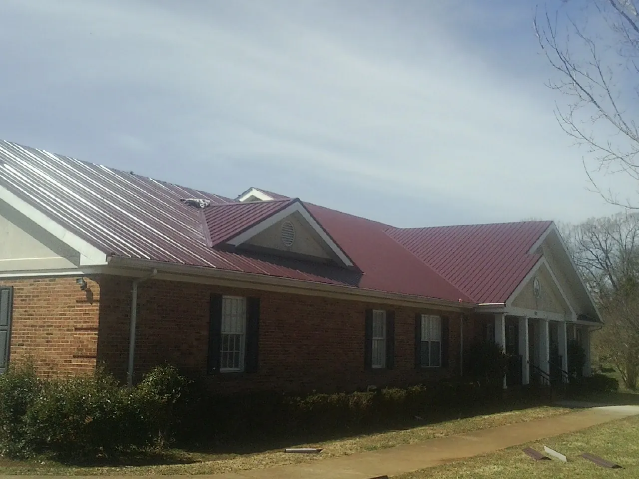 Red metal roof with gabled entries on a long brick building, from a Hail Damage Roof Repair job in Cape May