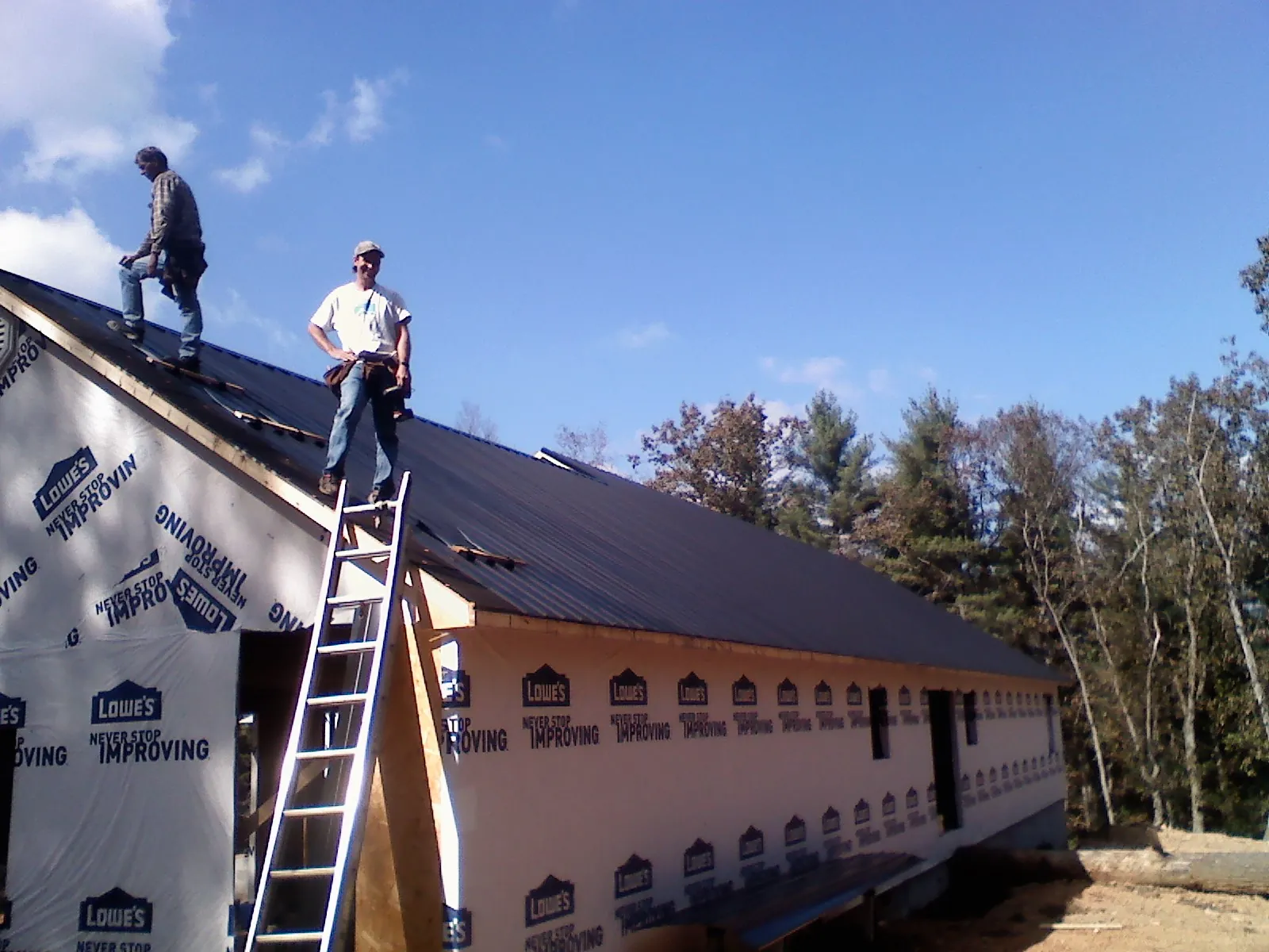 Two roofers standing on a long dark metal roof over a wrapped building in Cape May