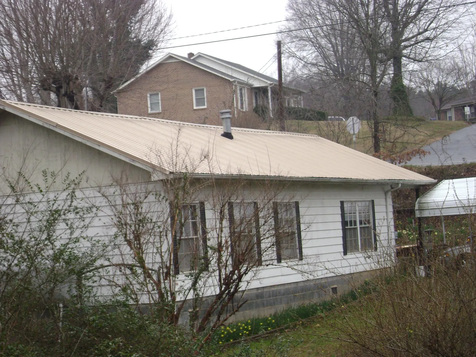 Tan metal roof on a white sided house set into a hillside — Commercial Roofing by Roofing Brothers in Cape May